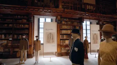 Mannequins wearing tailored coats and blazers displayed among placards in a wood-paneled historic library.
