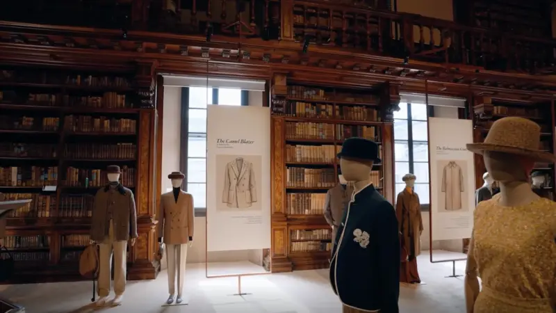 Mannequins wearing tailored coats and blazers displayed among placards in a wood-paneled historic library.
