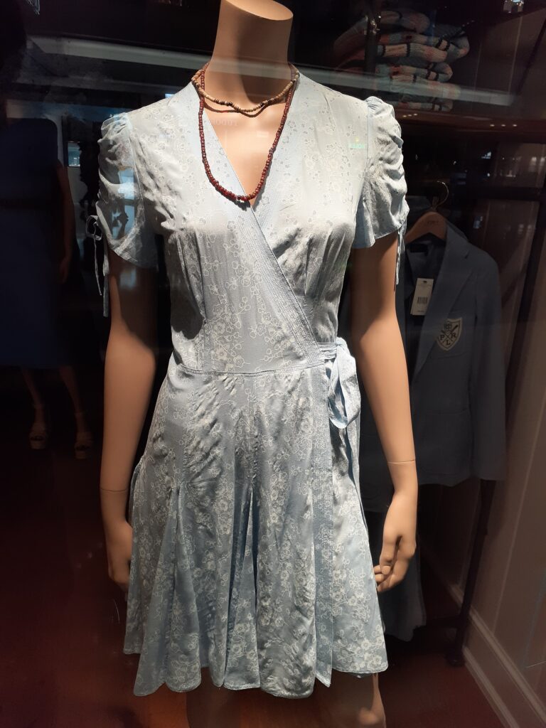 A mannequin wearing a pale blue floral wrap dress in a Ralph Lauren store display, with a Polo blazer visible nearby.