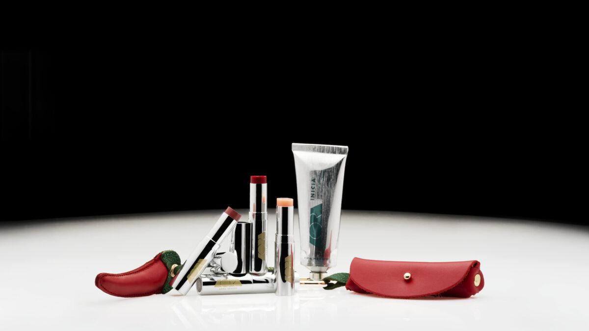 Silver lipstick tubes and a cream tube labeled AORA México displayed beside red leather chili-shaped pouches on a white surface.