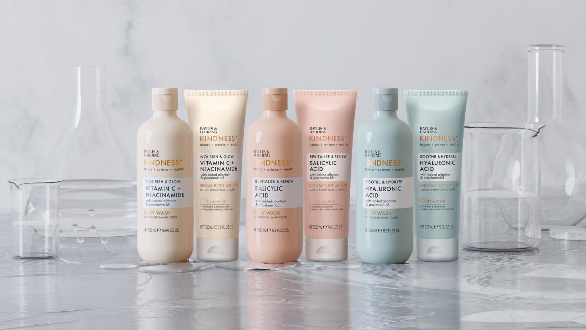 Six Baylis & Harding Kindness+ body wash and serum body lotion bottles arranged among laboratory glassware.