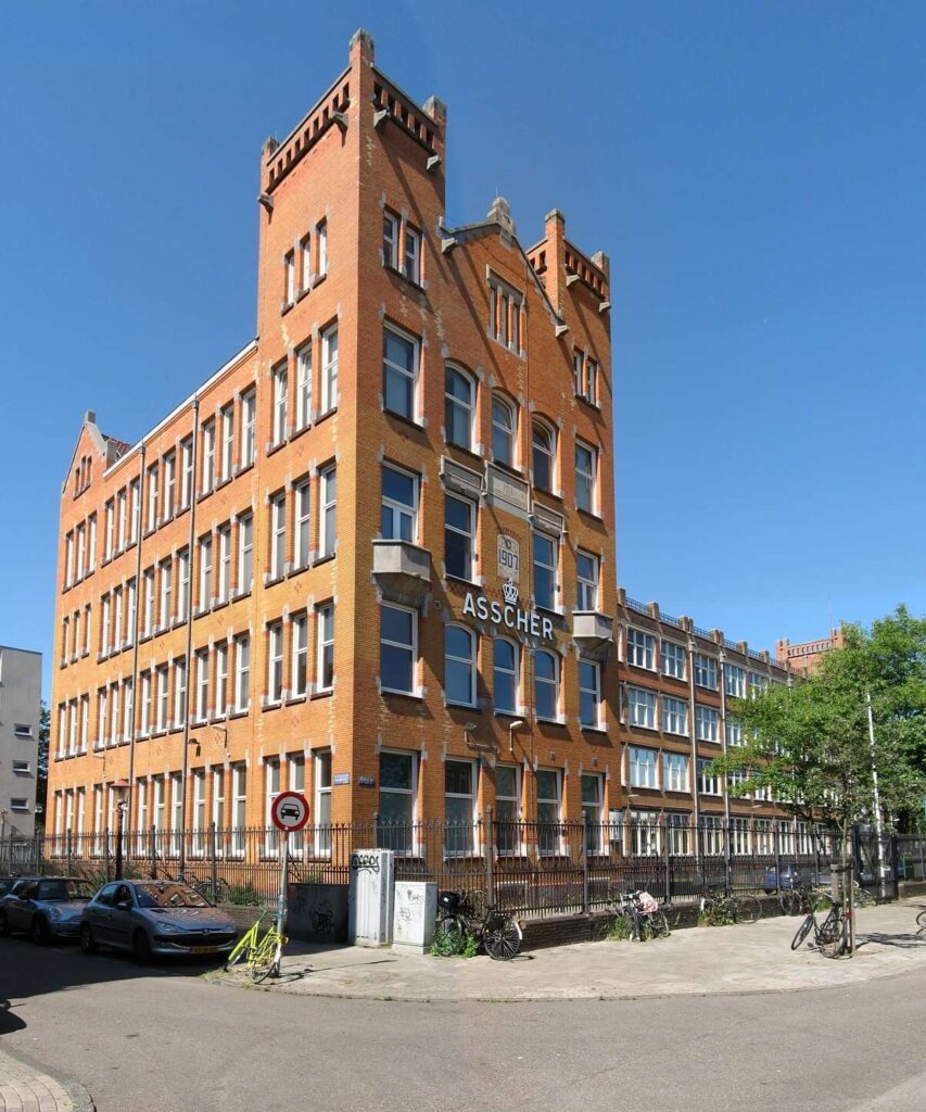 A brick building with the name ASSCHER and date 1907 inscribed on its facade, with bicycles parked outside.