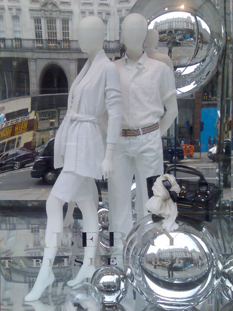 Burberry store window display featuring two mannequins in white outfits with reflective glass spheres and street reflection.