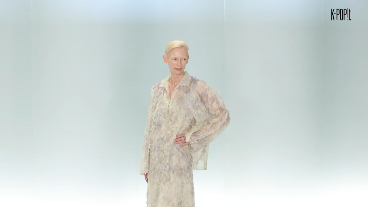 A woman with short blonde hair wears a feathery, textured Chanel outfit on a runway.