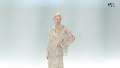 A woman with short blonde hair wears a feathery, textured Chanel outfit on a runway.