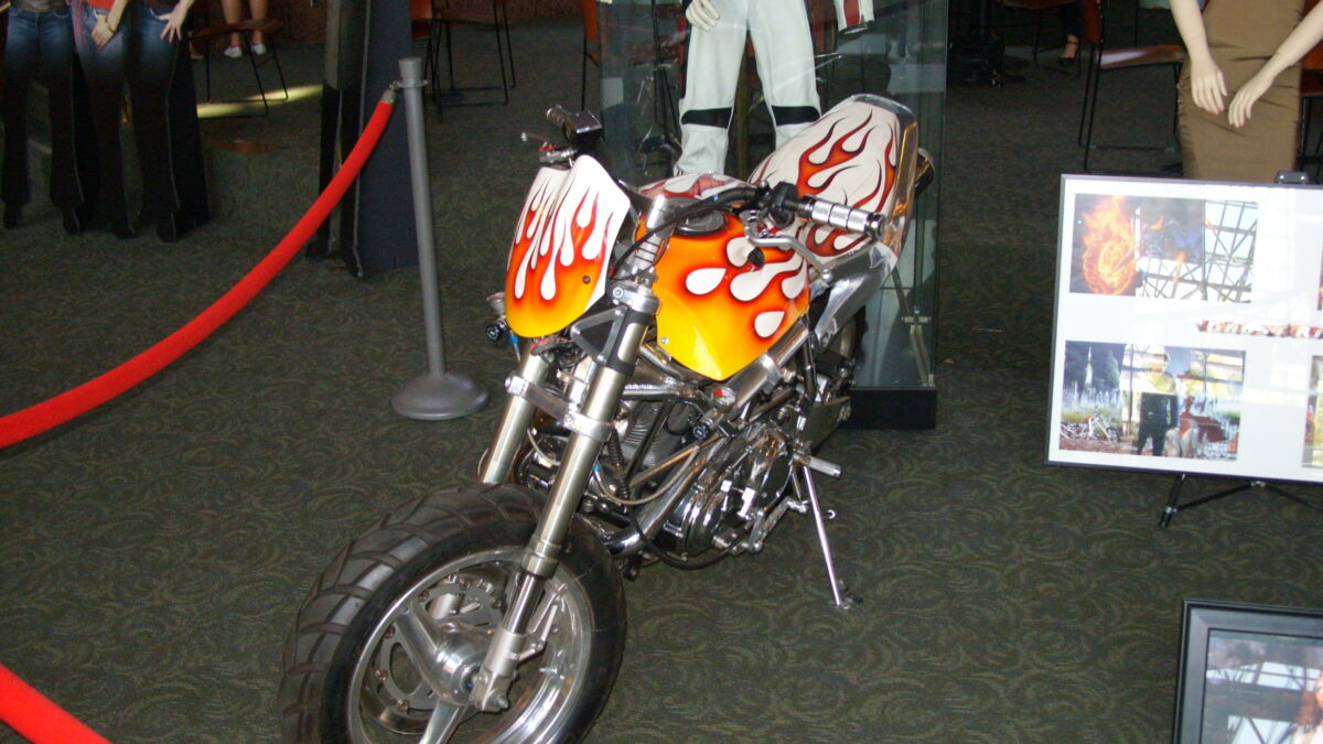 A flame-painted motorcycle prop from Ghost Rider displayed indoors behind a red rope barrier.