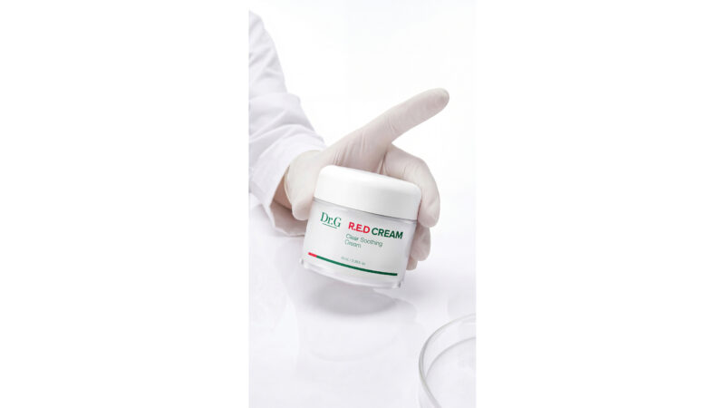 A gloved hand holds a jar of Dr.G R.E.D Cream against a white background.