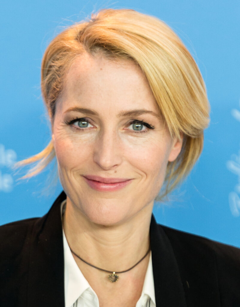 Close-up portrait of a blonde woman smiling in front of a blue backdrop.