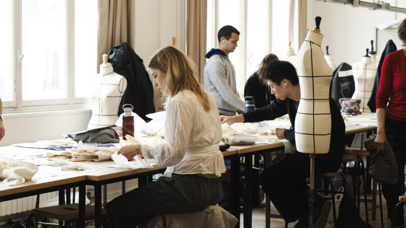 Students work at tables with fabric and dress forms in a bright fashion design classroom.