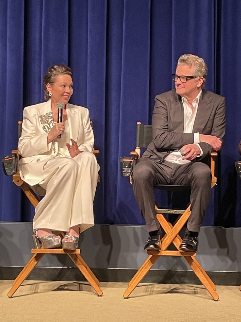 Olivia Colman and Colin Firth sit on director's chairs on stage during a Q&A session.