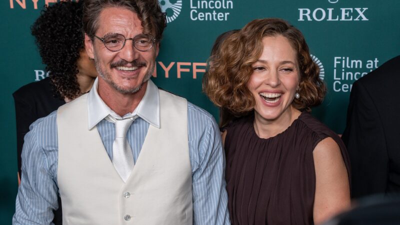 A man in a vest and tie and a woman in a dark dress smile together at a film festival step-and-repeat with NYFF and Rolex logos.