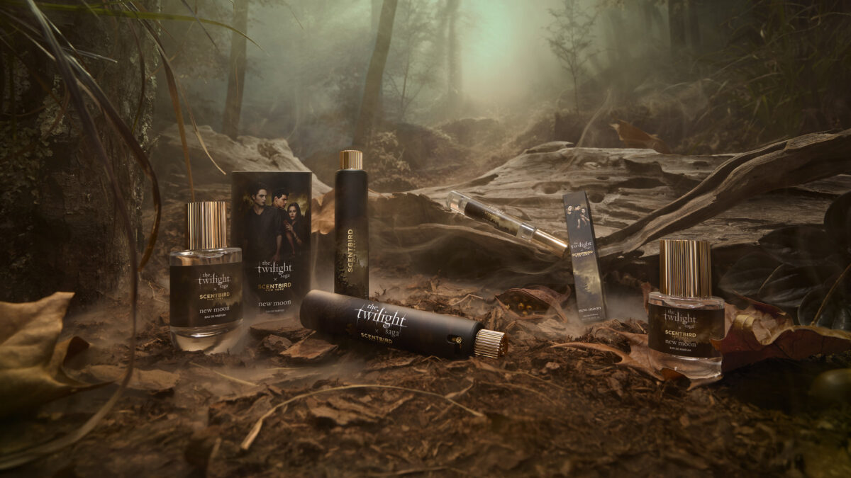 Twilight Saga New Moon Scentbird perfume bottles and boxes displayed on forest floor with misty trees in background.