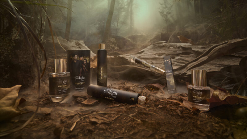 Twilight Saga New Moon Scentbird perfume bottles and boxes displayed on forest floor with misty trees in background.