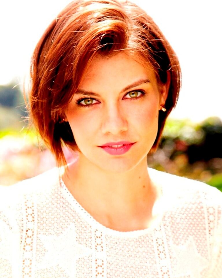 Close-up portrait of a woman with short reddish-brown hair wearing a white lace top outdoors.